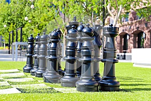 Giant black chess pieces on lush green grass surrounded by lush green trees and red brick buildings at Lenox Park
