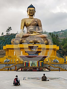 Giant Buddha statue in a serene pose above a temple with two people sitting in contemplation