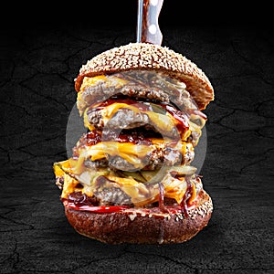 Giant burger with pork, bacon, jalapenos, marmalade onions and cucumber in a rye bun. Isolated on a dark background