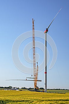 Giant construction site for a wind turbine, crane is lifting the second blade to install it onto the tower, heavy industry for