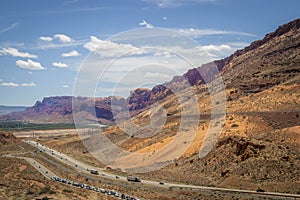 Giant geological fault near Moab Utah USA with highway full of cars and trucks and packed sideroad leading to Arches National Park