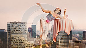 Giant image of happy, smiling, beautiful young woman standing on city background, laughing and drinking cocktail