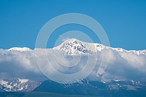 Giant mountains with snow above white clouds in sunny day. Glacier under blue sky. Amazing snowy mountain landscape of majestic