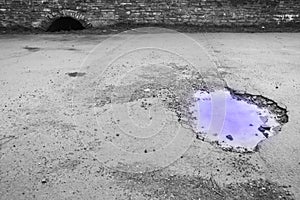 Giant pot hole in road with violet water and contrasting black and white background