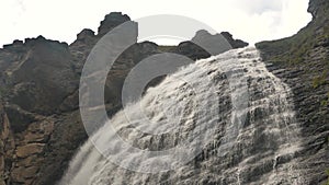 Giant waterfall flows down from a high mountain, water flows over a smooth rock slow motion, view from below