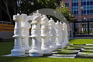 Giant white chess pieces on lush green grass surrounded by lush green trees and red brick buildings at Lenox Park