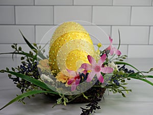 Giant yellow Easter Egg shimmery, sitting in a spring wreath with pink, purple and yellow flowers, on a sandstone counter with a