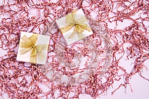 Gift for beloved woman. Top view of two small wrapped gift boxes with golden bows on pastel pink background with