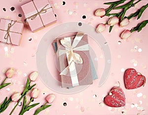 Gift books bandaged with a pink ribbon bow surrounded by tulips, confetti and hearts on pink background