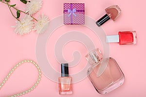 Gift box, beads, bottle of perfume, bottles with nail polish and flowers on a pink background.