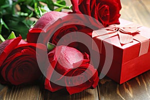 Gift box and beautiful roses on wooden background, closeup