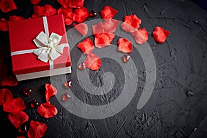 Gift box on black stone table. Romantic holiday background with rose petals