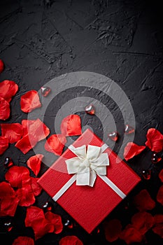 Gift box on black stone table. Romantic holiday background with rose petals