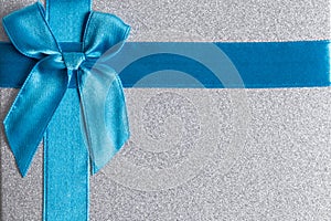 Gift box with blue satin ribbon and bow on grey background.