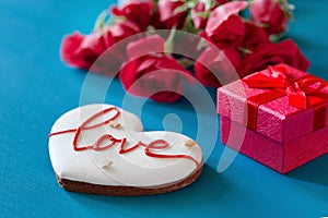 Gift box and bouquet of roses and gingerbread in the shape of heart with the inscription love for holiday on wooden