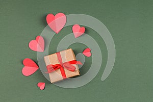 Gift box with bow and paper hearts on a green background.