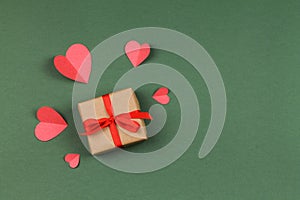 Gift box with bow and paper hearts on a green background.
