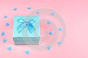 Gift box with a bow on a pink background with hearts confetti