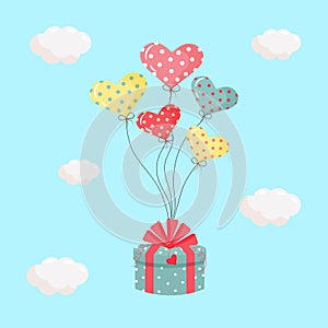 Gift box with a bow tied to heart inflatable gel balloons in the sky. Birthday party or Valentine\'s day concept