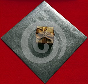 Gift box in bronze color with a bow and a black craft envelope on a red background