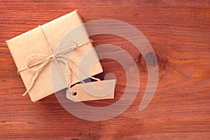 Gift box into brown paper tied by twine with blank tag on old wooden table with space for text