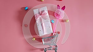 Gift box, chocolate Easter eggs and shopping cart on a pink background.