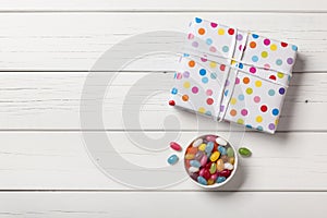 Gift box and colorful candies on white wooden background