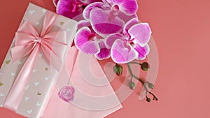 Gift box, envelope and orchid branch on a pink background.