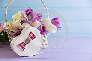 Gift box in form of heart with basket full of purple and white tulips on tender wooden background