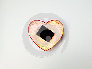 Gift box in the form of a heart with lights inside, a black jewelry box and wrapping paper on a white background