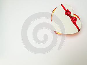 Gift box in the form of a heart with a red ribbon with a bow ajar with lights inside on a white background