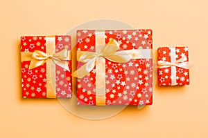 Gift box with gold bow for Christmas or New Year day on orange background, top view