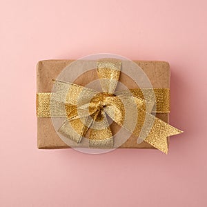 Gift box with golden ribbon on pink pastel background with space. Minimal cincept of holiday. Top view.