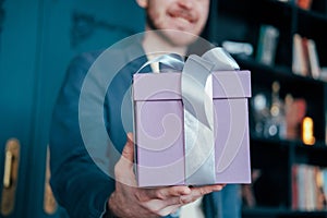 Gift box with gray silver ribbon in the hands of young attracrive man on blue background