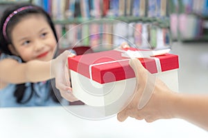 Gift box for kids girl. White box with red bow in the smiling asian girl hands for give a gift in the library.