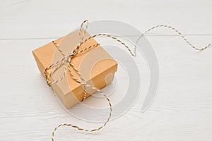 Gift box on kraft paper with a rope bow is on a white wooden table, with place for your text