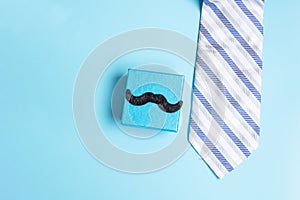 Gift box with mustache and necktie on blue background, preparation for fathers. World International men day and Fatherâ€™s day