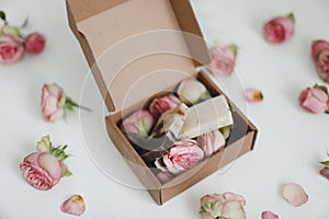 Gift box with natural homemade soap bars and rose flowers on white background. Holiday gift, opening present, top view.