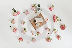 Gift box with natural homemade soap bars and rose flowers on white background. Holiday gift, opening present, top view.