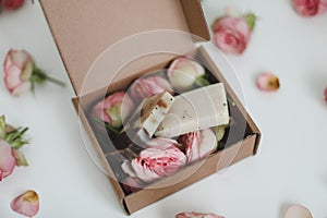 Gift box with natural homemade soap bars and rose flowers on white background. Holiday gift, opening present, top view.