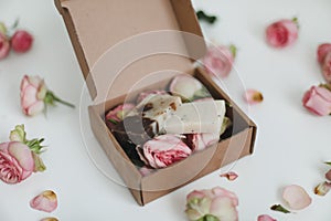 Gift box with natural homemade soap bars and rose flowers on white background. Holiday gift, opening present, top view.