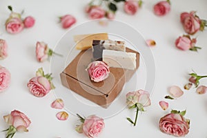 Gift box with natural homemade soap bars and rose flowers on white background. Holiday gift, opening present, top view.