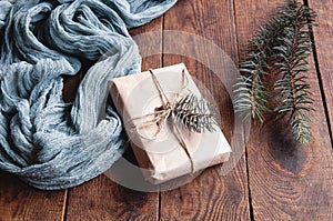Gift box next to vintage tablecloth gray and christmas tree leaves on wooden brown table