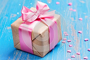 Gift box with pink bow ribbon and glitter hearts on blue spring background