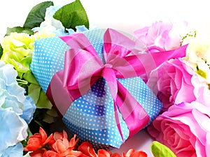 Gift box with pink ribbon bow and beautiful colorful flowers background