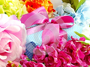 Gift box with pink ribbon bow and beautiful colorful flowers background