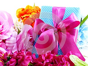 Gift box with pink ribbon bow and beautiful colorful flowers background