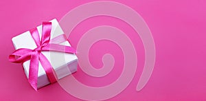 Gift box with pink ribbon on pink background