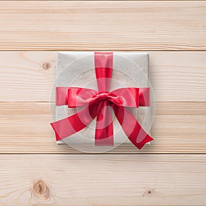 Gift box present isolated with clipping path with red bow satin ribbon over brown wrapping paper on white pine wood background