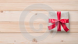 Gift box present isolated with clipping path with red bow satin ribbon over brown wrapping paper on white pine wood background f